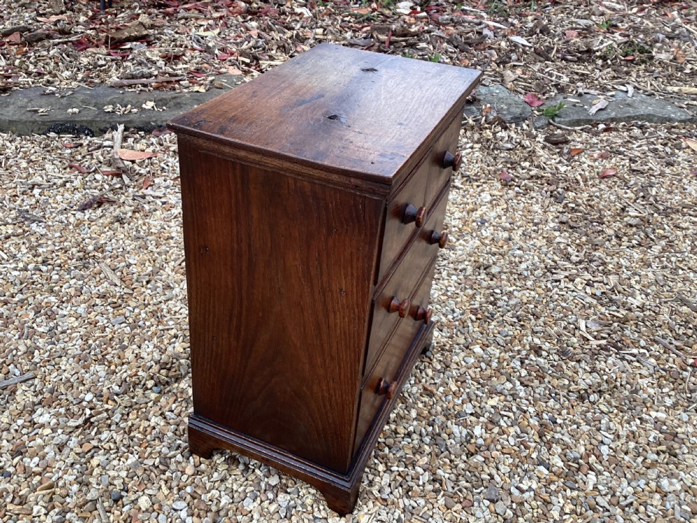 A small Georgian style miniature wooden chest of drawers featuring two short drawers over two long drawers with turned wooden knobs and bracket feet. View V