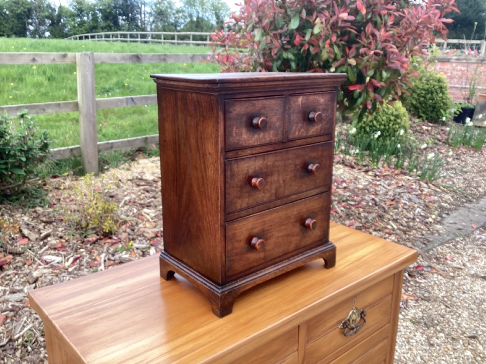 A small Georgian style miniature wooden chest of drawers featuring two short drawers over two long drawers with turned wooden knobs and bracket feet. View VI