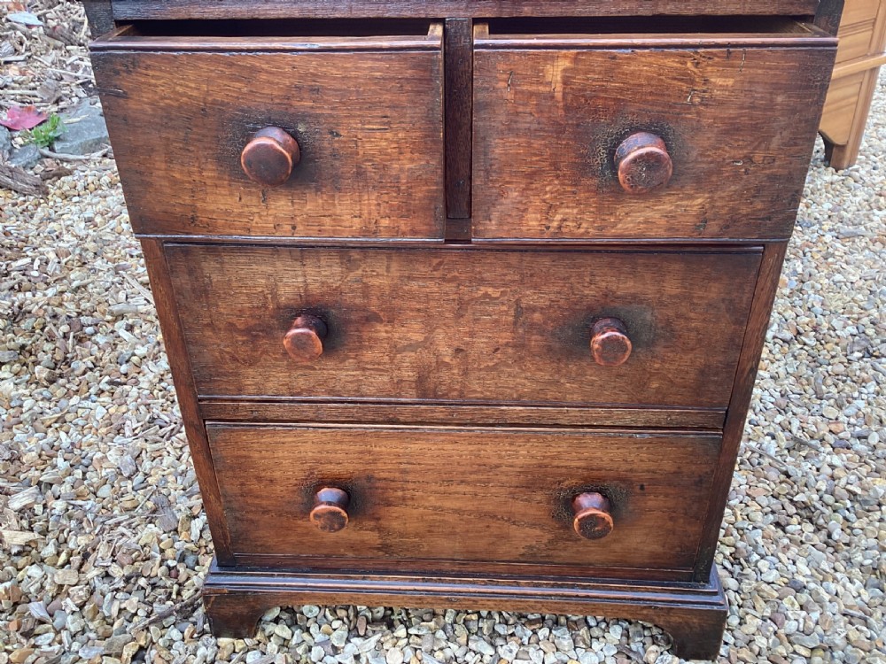 A small Georgian style miniature wooden chest of drawers featuring two short drawers over two long drawers with turned wooden knobs and bracket feet. View X