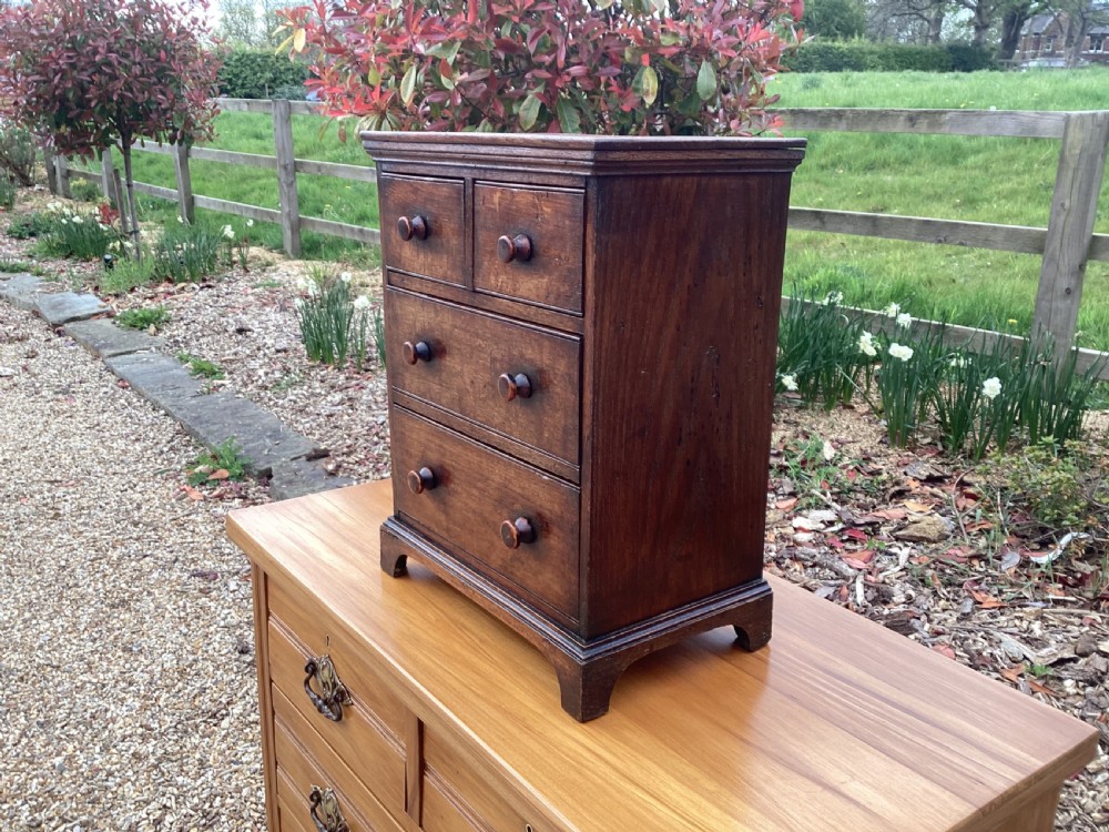 A small Georgian style miniature wooden chest of drawers featuring two short drawers over two long drawers with turned wooden knobs and bracket feet. View XI