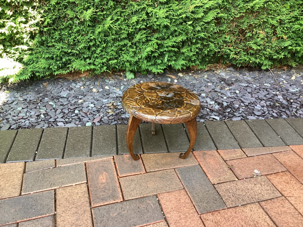 A low circular wooden plant stand featuring hand-carved floral motifs on the surface and curved legs.