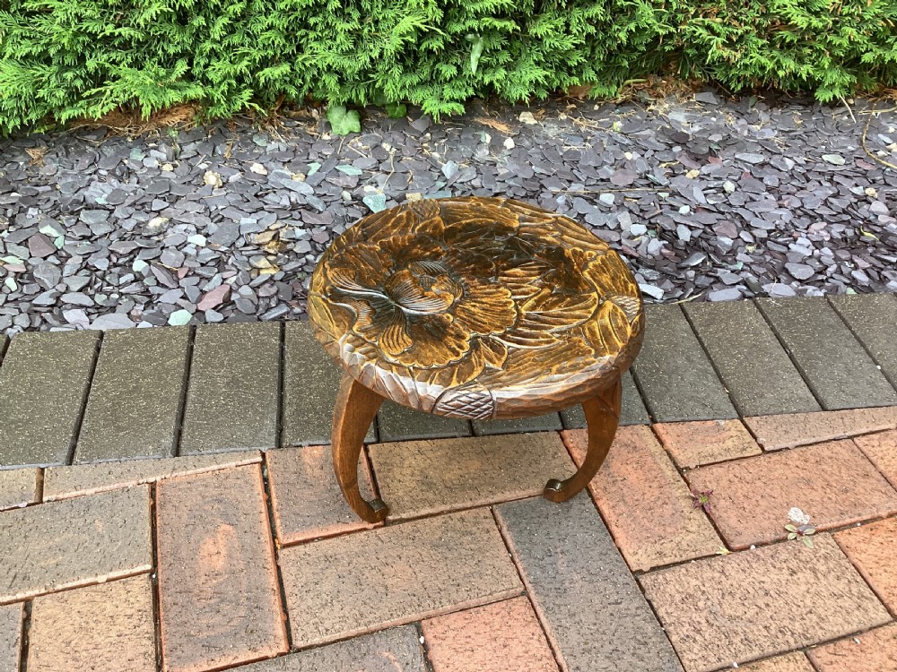 A low circular wooden plant stand featuring hand-carved floral motifs on the surface and curved legs. View II