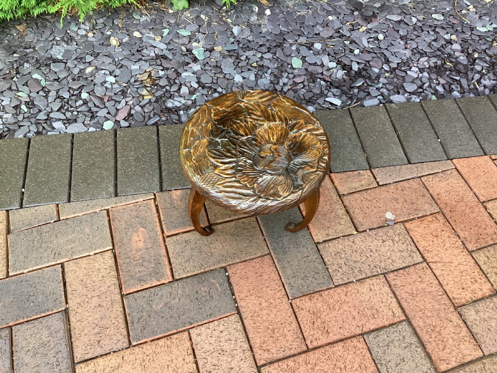 A low circular wooden plant stand featuring hand-carved floral motifs on the surface and curved legs. View III
