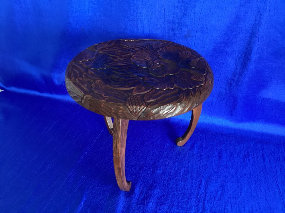 A low circular wooden plant stand featuring hand-carved floral motifs on the surface and curved legs. View VII