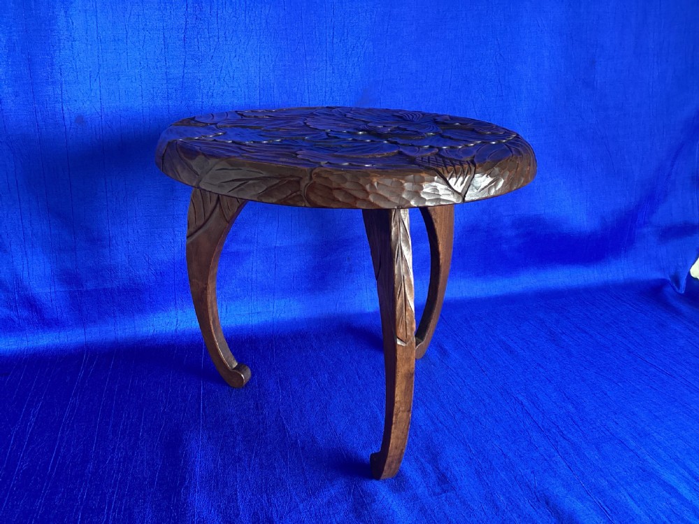A low circular wooden plant stand featuring hand-carved floral motifs on the surface and curved legs. View VIII