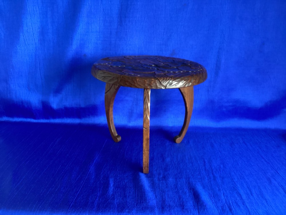 A low circular wooden plant stand featuring hand-carved floral motifs on the surface and curved legs. View X