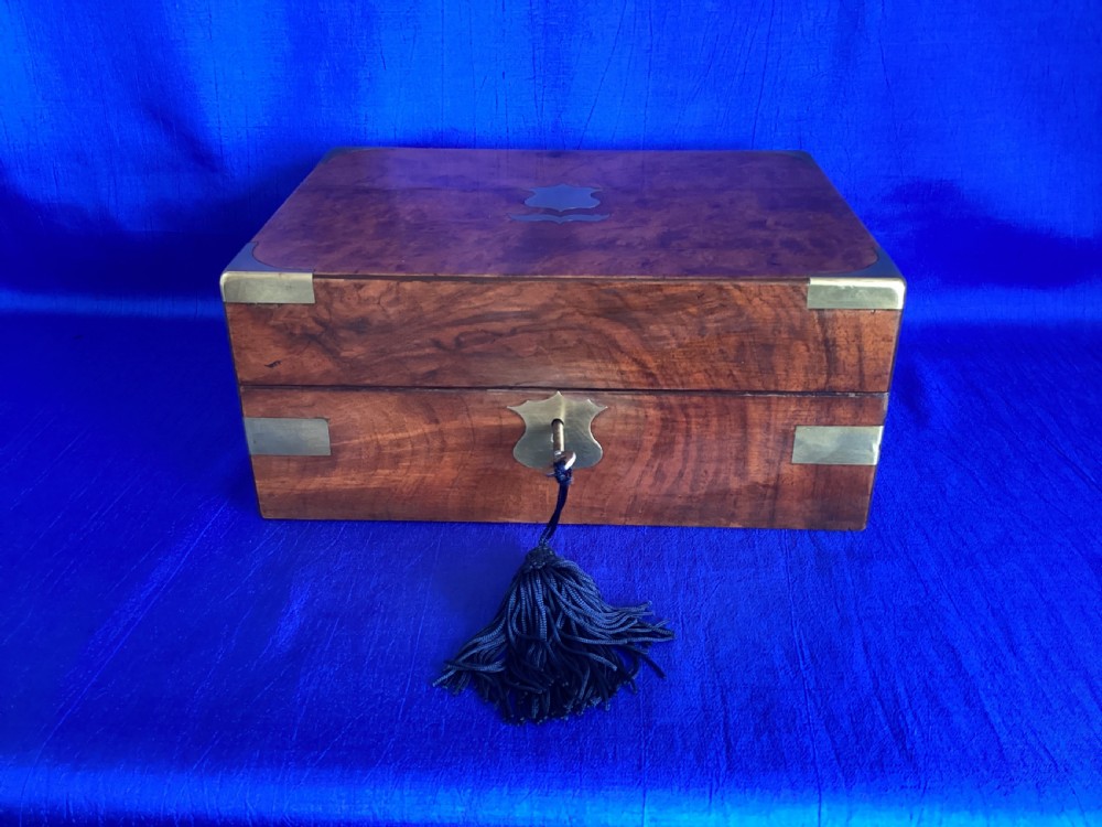 A rectangular Victorian walnut wooden box featuring protective brass corner brackets, a central keyhole escutcheon plate, and an inlaid lid cartouche.