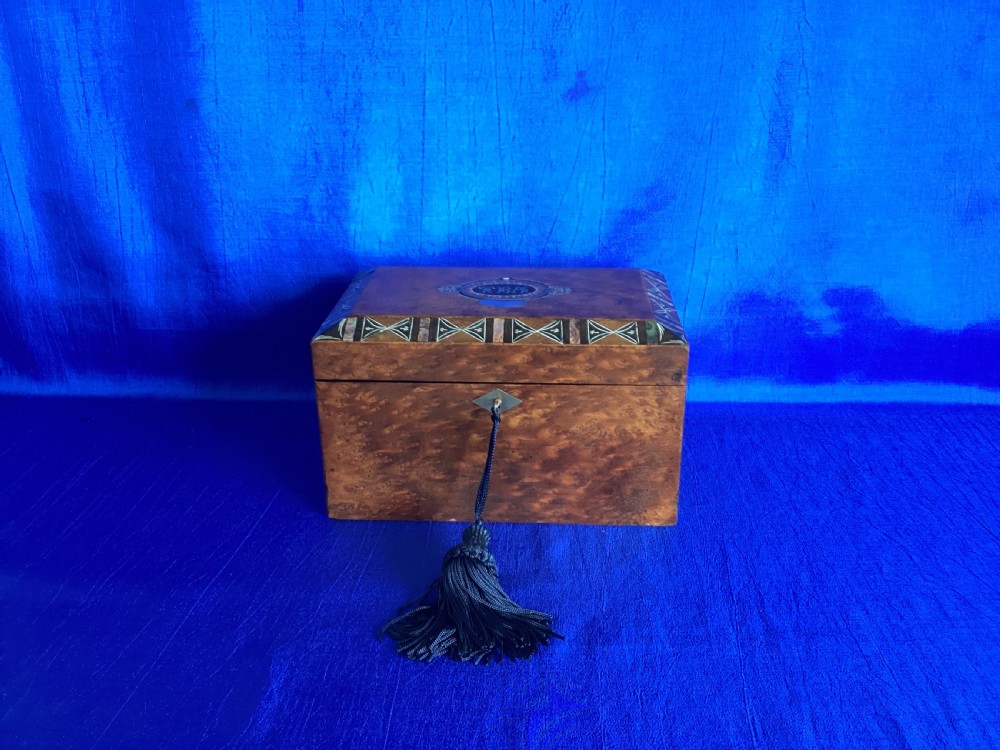 A rectangular Georgian burr walnut tea caddy featuring geometric inlaid borders on the lid and a key with a black tassel.