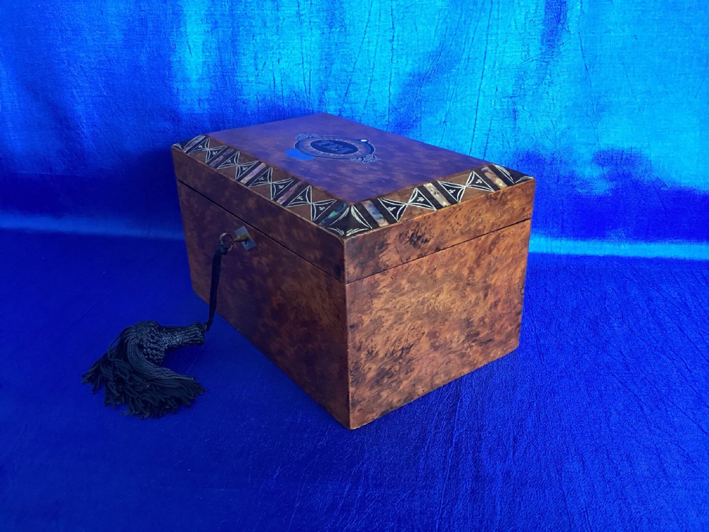 A rectangular Georgian burr walnut tea caddy featuring geometric inlaid borders on the lid and a key with a black tassel. View II