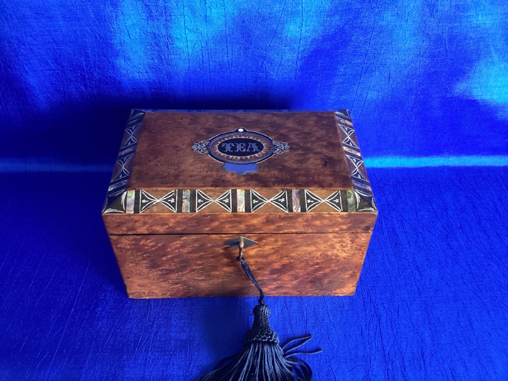 A rectangular Georgian burr walnut tea caddy featuring geometric inlaid borders on the lid and a key with a black tassel. View IV