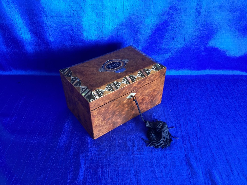 A rectangular Georgian burr walnut tea caddy featuring geometric inlaid borders on the lid and a key with a black tassel. View IX