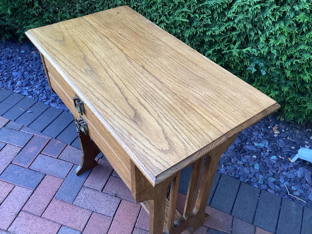 An antique light oak Jugendstil side table featuring two drawers with rectangular brass drop handles, flared side supports, and a lower shelf. View II