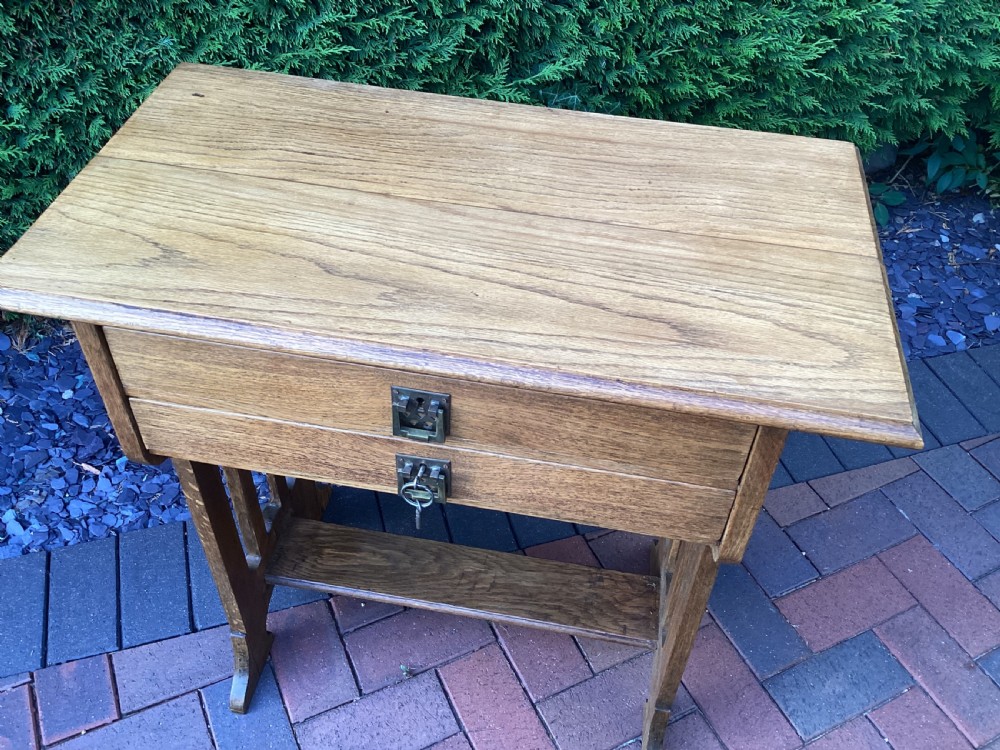 An antique light oak Jugendstil side table featuring two drawers with rectangular brass drop handles, flared side supports, and a lower shelf. View IV