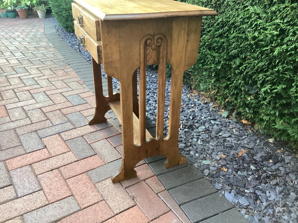 An antique light oak Jugendstil side table featuring two drawers with rectangular brass drop handles, flared side supports, and a lower shelf. View VII