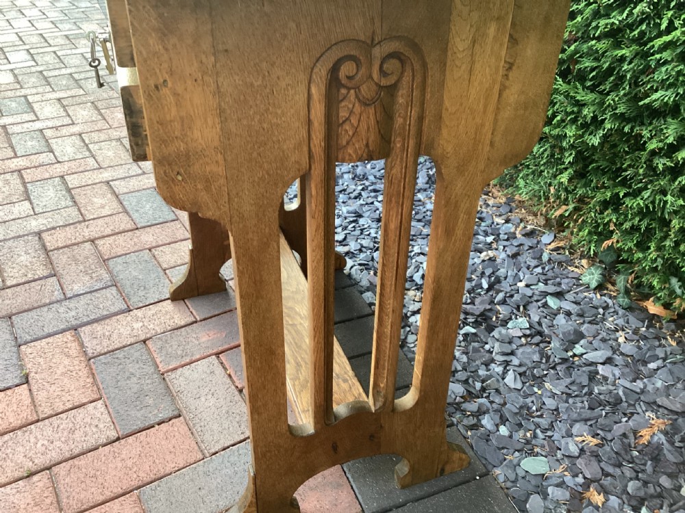 An antique light oak Jugendstil side table featuring two drawers with rectangular brass drop handles, flared side supports, and a lower shelf. View VIII