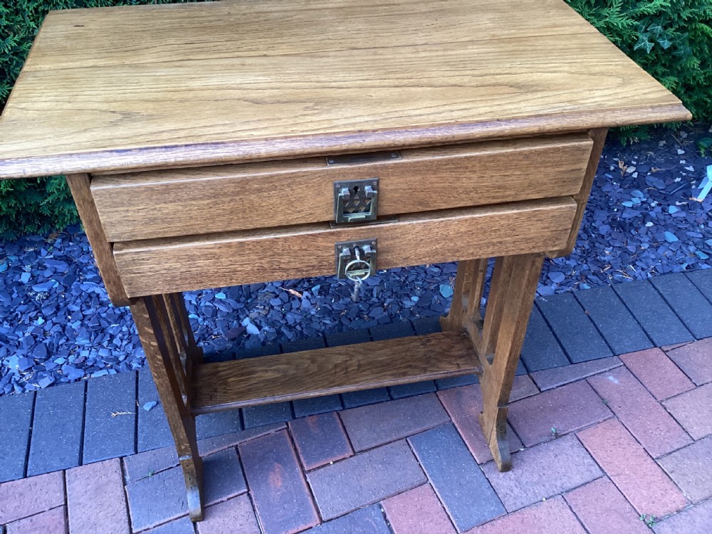 An antique light oak Jugendstil side table featuring two drawers with rectangular brass drop handles, flared side supports, and a lower shelf. View IX