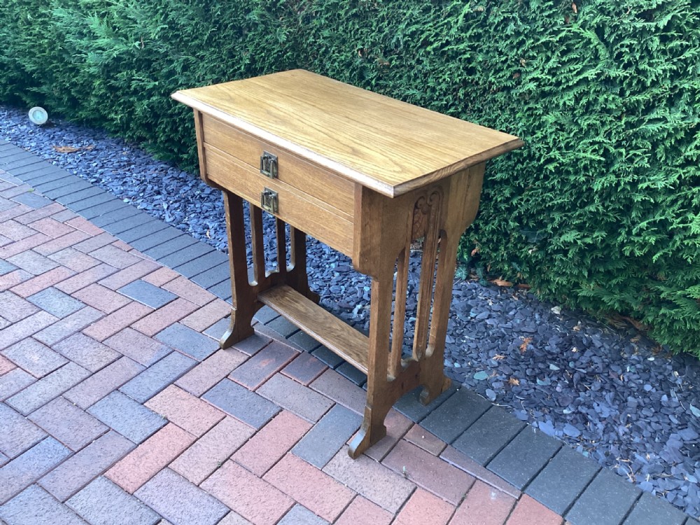 An antique light oak Jugendstil side table featuring two drawers with rectangular brass drop handles, flared side supports, and a lower shelf. View XI