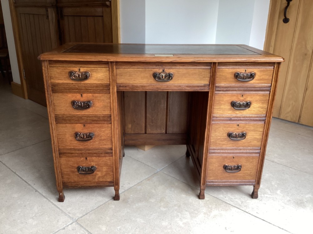 An Edwardian oak twin pedestal desk with nine drawers featuring brass handles and a leather writing surface insert.