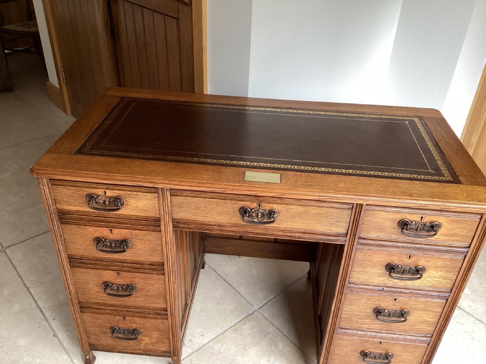 An Edwardian oak twin pedestal desk with nine drawers featuring brass handles and a leather writing surface insert. View II