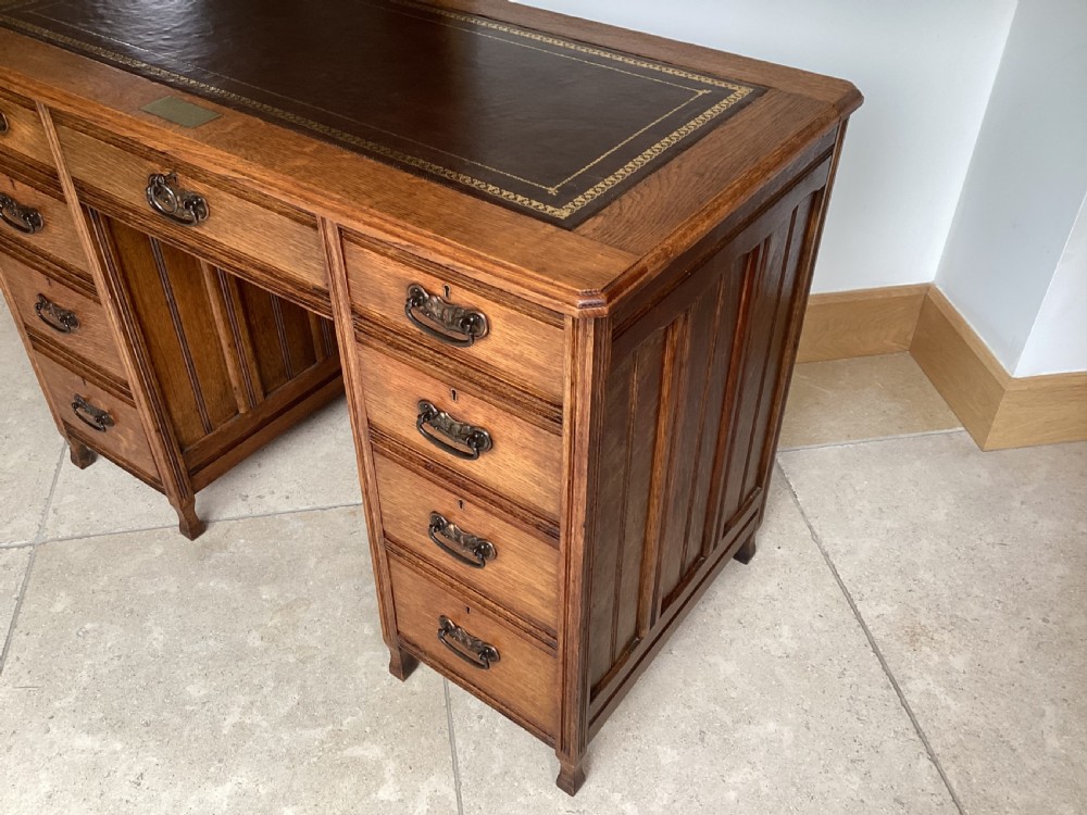 An Edwardian oak twin pedestal desk with nine drawers featuring brass handles and a leather writing surface insert. View V