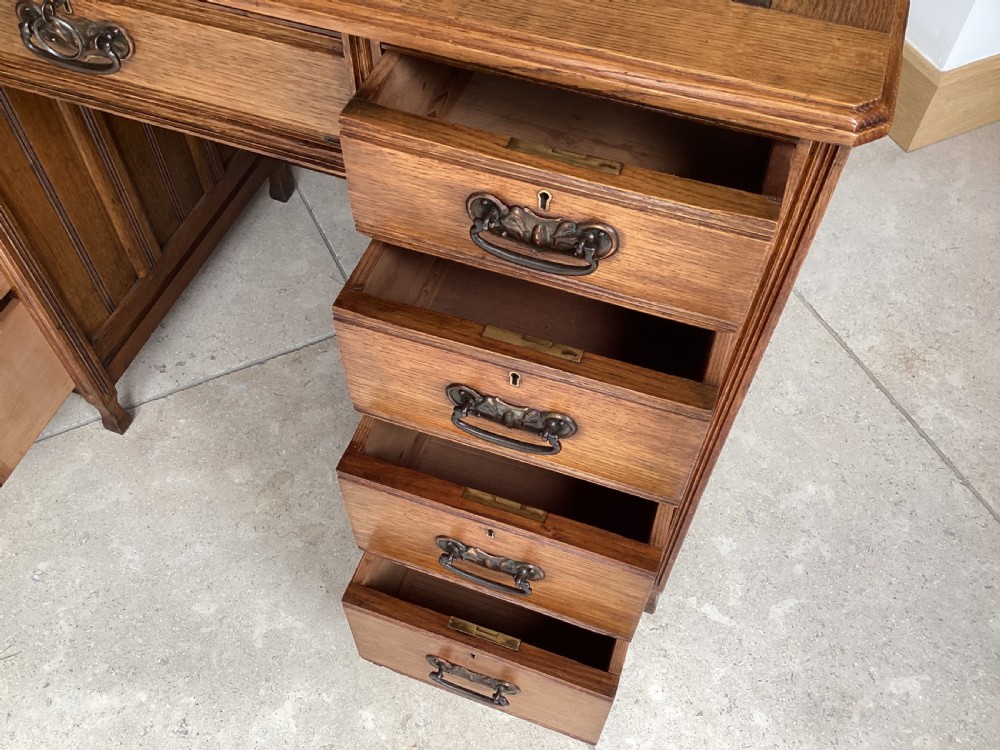 An Edwardian oak twin pedestal desk with nine drawers featuring brass handles and a leather writing surface insert. View VII