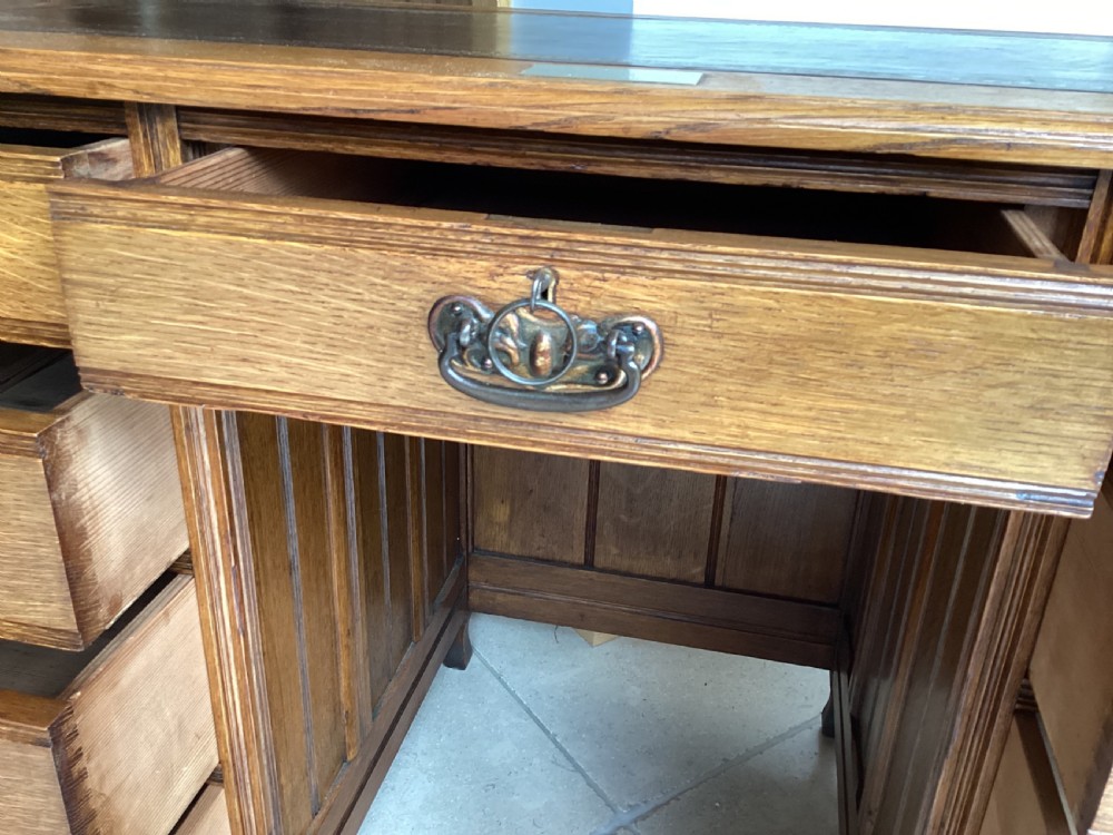 An Edwardian oak twin pedestal desk with nine drawers featuring brass handles and a leather writing surface insert. View VIII