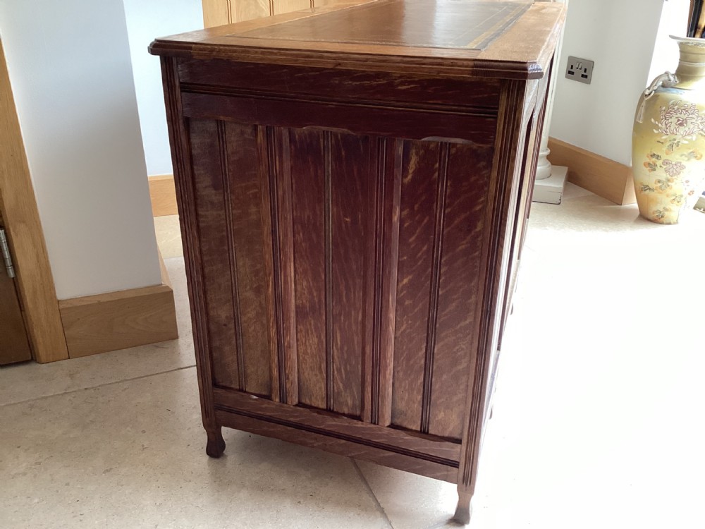 An Edwardian oak twin pedestal desk with nine drawers featuring brass handles and a leather writing surface insert. View X