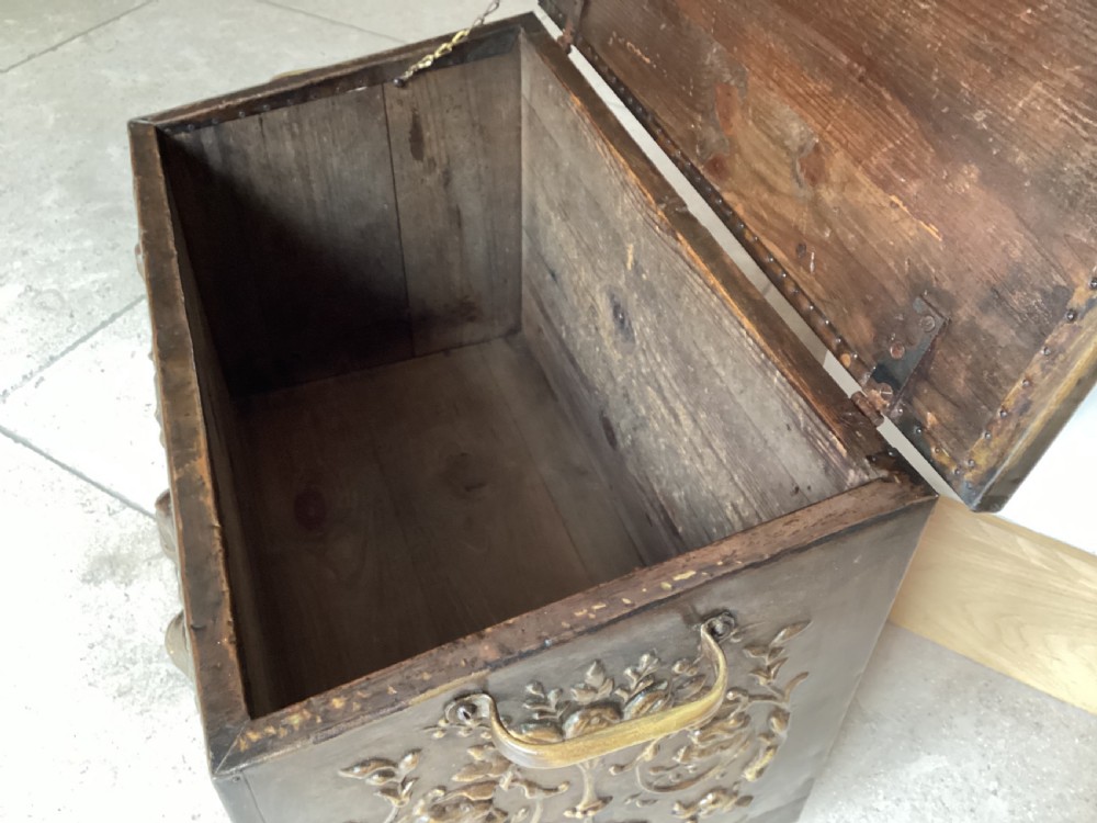 An antique brass-clad wooden fireside log box featuring embossed relief scenes of figures in a tavern on the front and foliate scrollwork on the lid. View IX