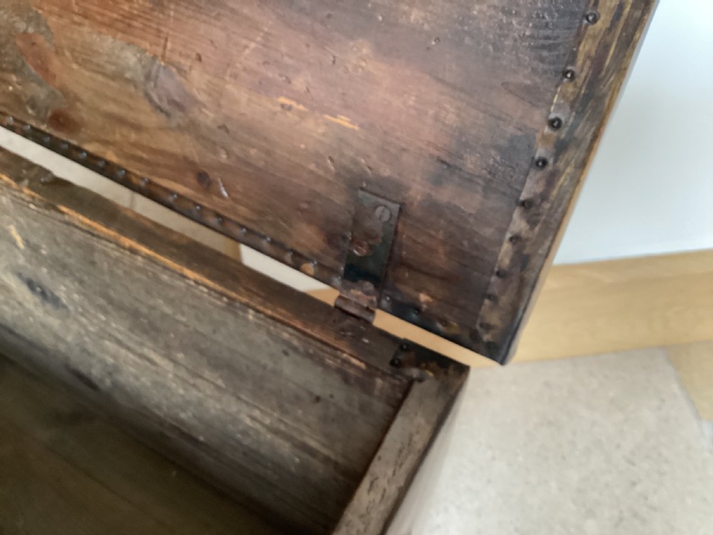 An antique brass-clad wooden fireside log box featuring embossed relief scenes of figures in a tavern on the front and foliate scrollwork on the lid. View X