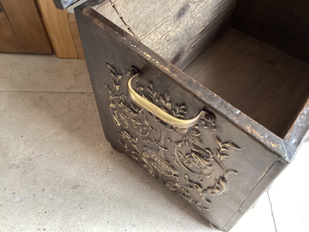 An antique brass-clad wooden fireside log box featuring embossed relief scenes of figures in a tavern on the front and foliate scrollwork on the lid. View XII