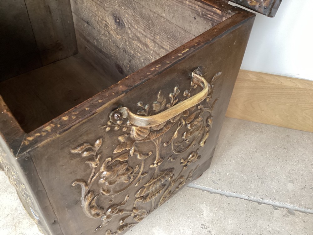 An antique brass-clad wooden fireside log box featuring embossed relief scenes of figures in a tavern on the front and foliate scrollwork on the lid. View XIII