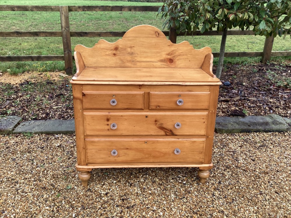 A Victorian honey pine chest of drawers featuring a shaped gallery upstand, clear glass knobs, and turned feet.