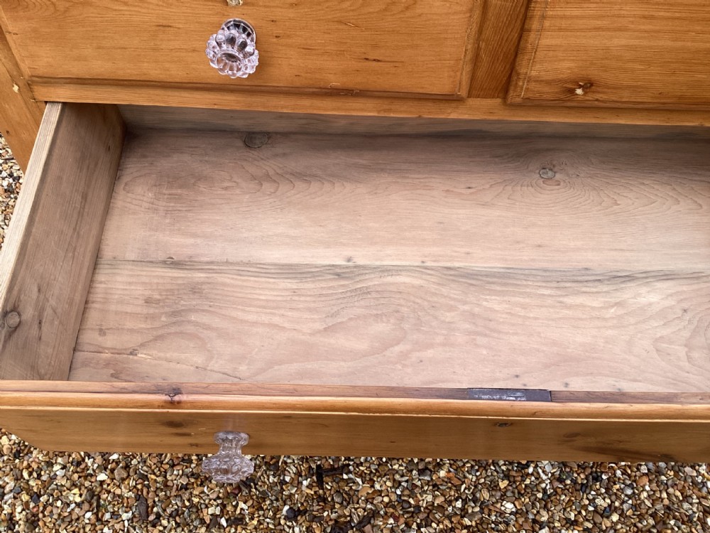 A Victorian honey pine chest of drawers featuring a shaped gallery upstand, clear glass knobs, and turned feet. View IV