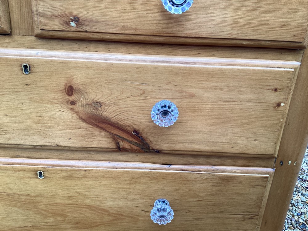 A Victorian honey pine chest of drawers featuring a shaped gallery upstand, clear glass knobs, and turned feet. View VI