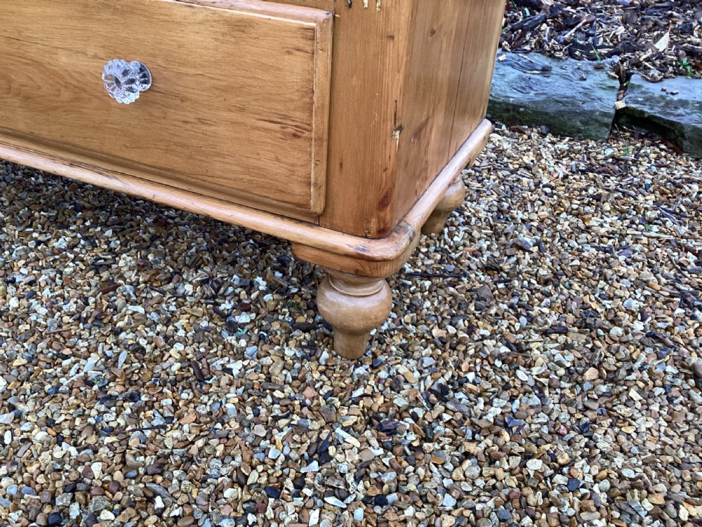 A Victorian honey pine chest of drawers featuring a shaped gallery upstand, clear glass knobs, and turned feet. View IX