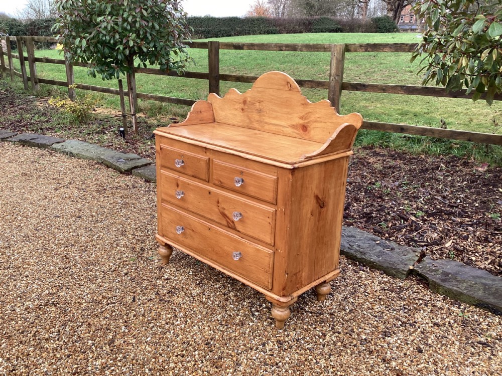 A Victorian honey pine chest of drawers featuring a shaped gallery upstand, clear glass knobs, and turned feet. View X