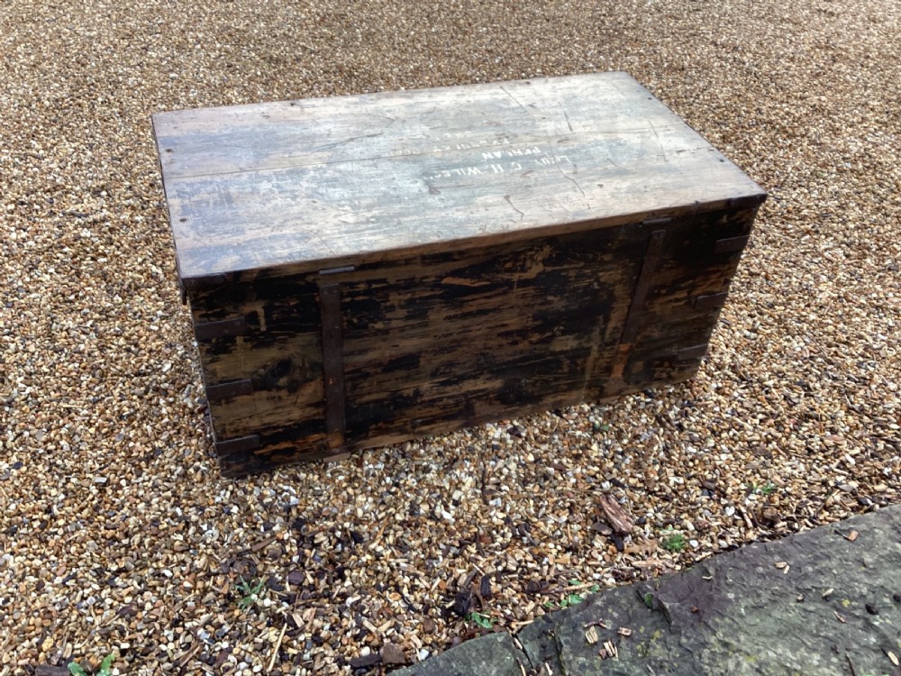 A rectangular antique dark wood military campaign chest featuring stencilled white lettering and iron strap reinforcements. View X