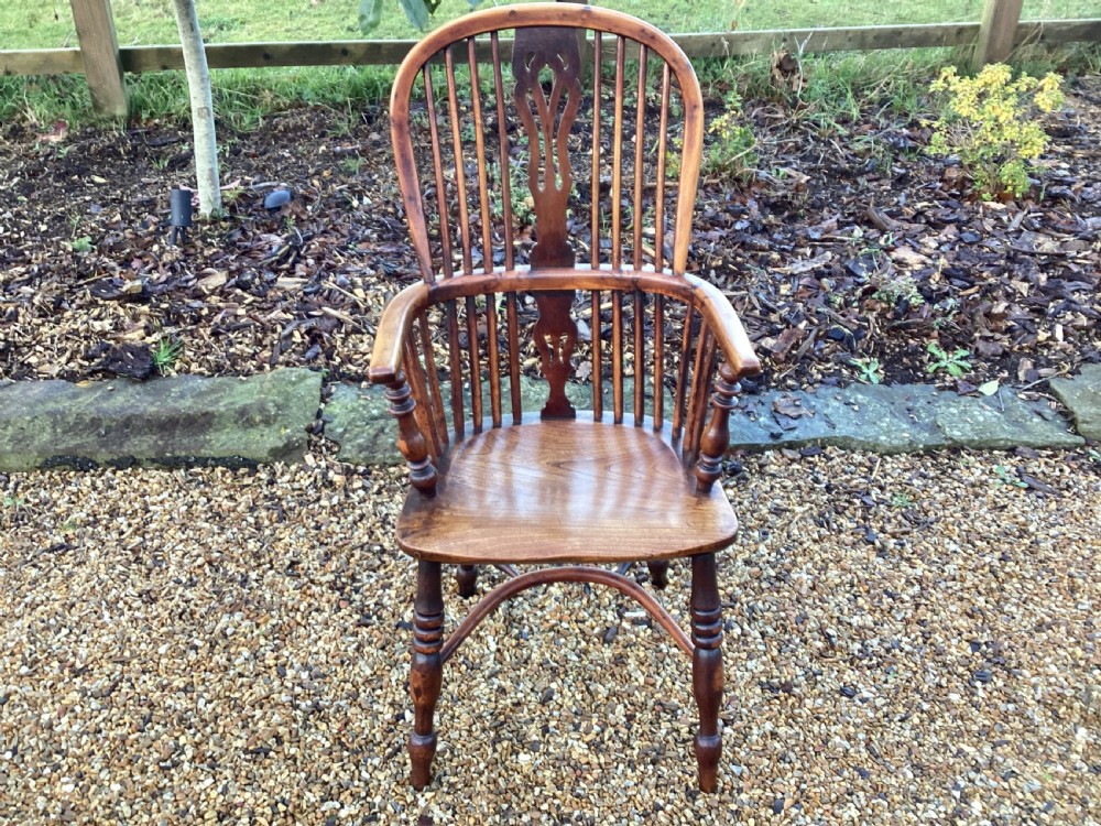 A wooden Georgian Windsor armchair featuring a hoop back, central pierced splat, vertical spindles, shaped seat, turned legs, and curved armrests.