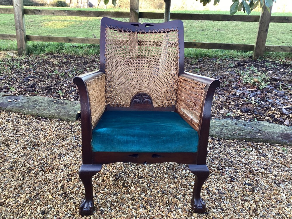 A dark mahogany Art Deco bergere armchair featuring fan pattern cane backrest weaving, cane side panels, cabriole legs, and a rich teal velvet seat cushion.
