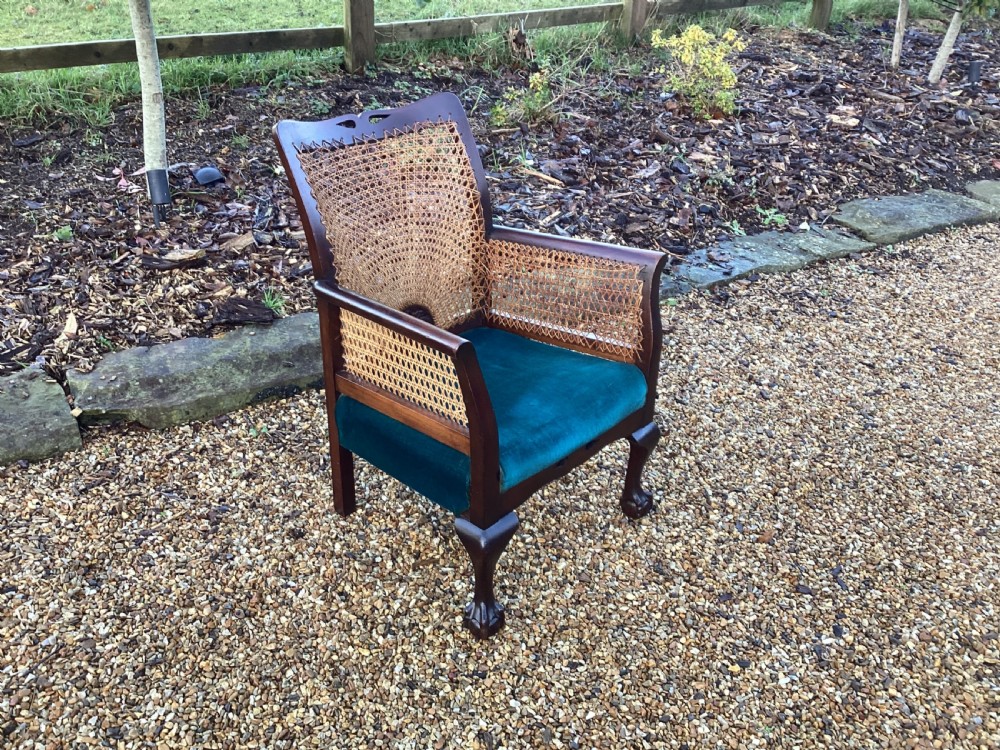 A dark mahogany Art Deco bergere armchair featuring fan pattern cane backrest weaving, cane side panels, cabriole legs, and a rich teal velvet seat cushion. View II
