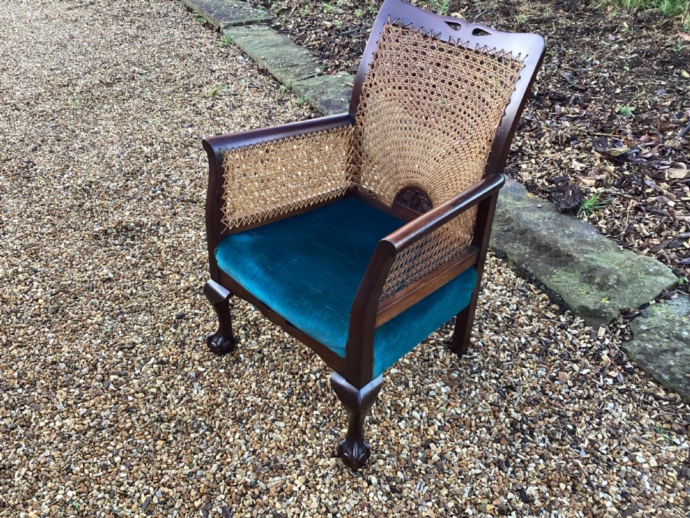 A dark mahogany Art Deco bergere armchair featuring fan pattern cane backrest weaving, cane side panels, cabriole legs, and a rich teal velvet seat cushion. View III