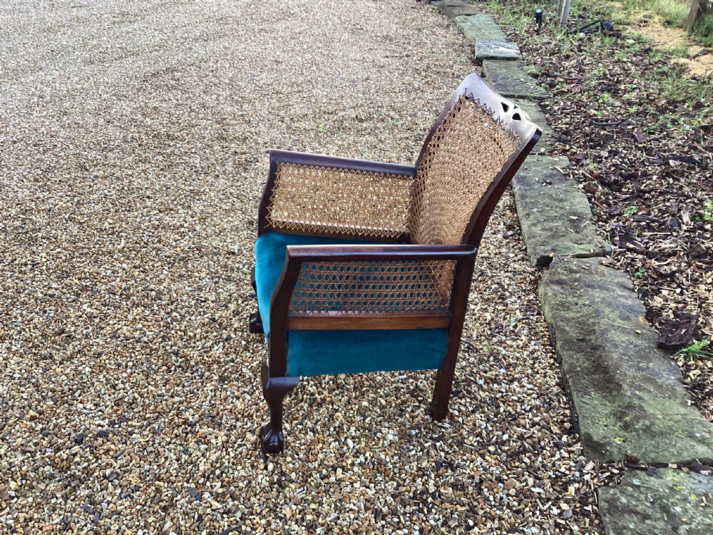 A dark mahogany Art Deco bergere armchair featuring fan pattern cane backrest weaving, cane side panels, cabriole legs, and a rich teal velvet seat cushion. View VI