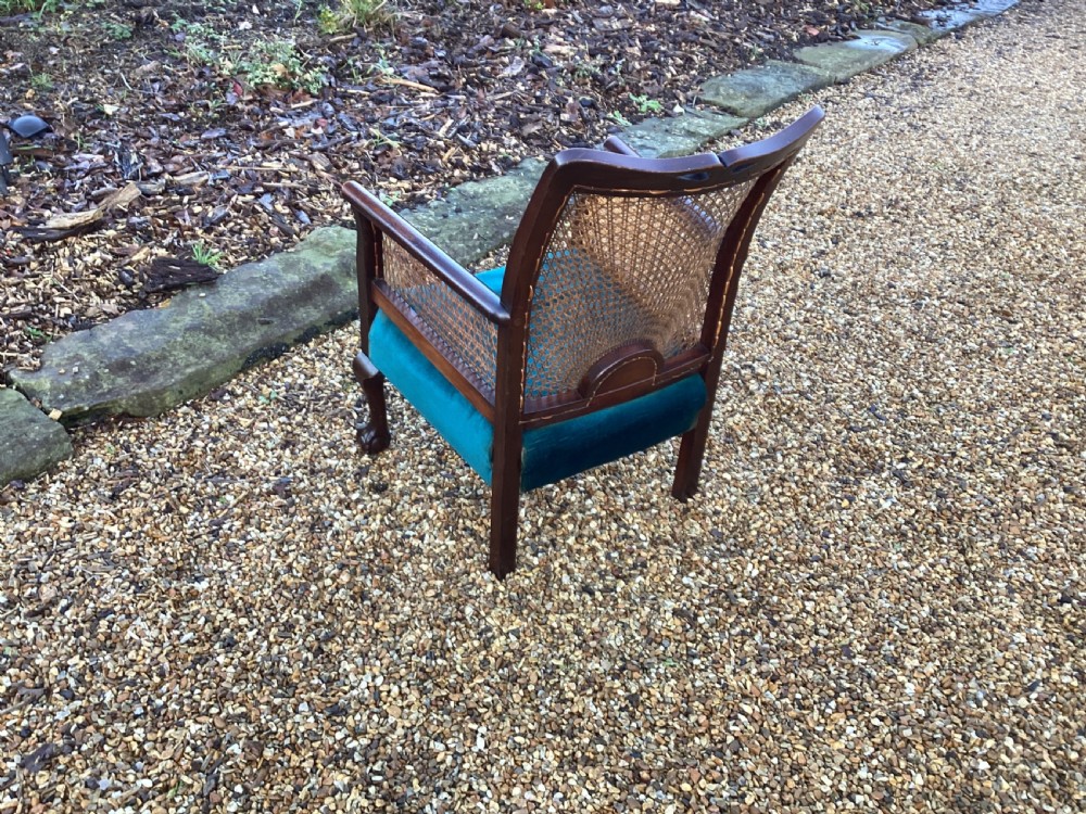 A dark mahogany Art Deco bergere armchair featuring fan pattern cane backrest weaving, cane side panels, cabriole legs, and a rich teal velvet seat cushion. View VII