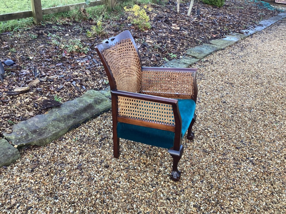 A dark mahogany Art Deco bergere armchair featuring fan pattern cane backrest weaving, cane side panels, cabriole legs, and a rich teal velvet seat cushion. View X