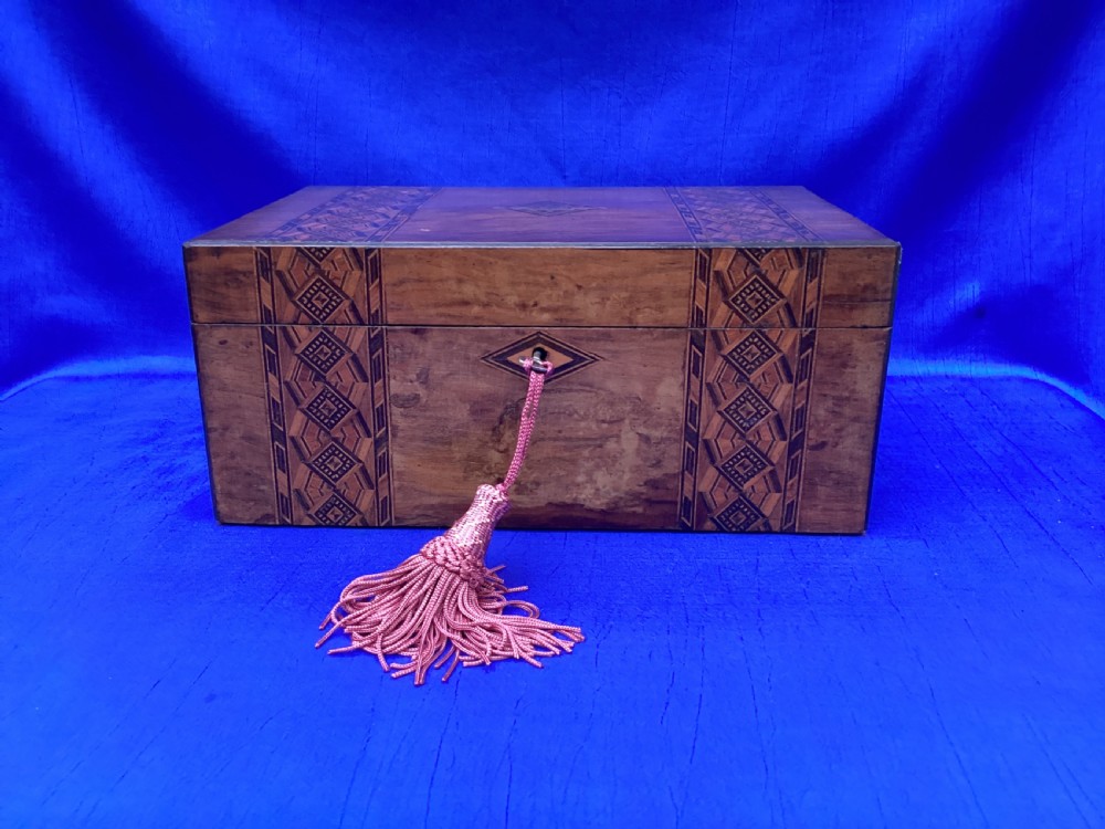 A rectangular Victorian walnut keepsake box featuring geometric parquetry inlay bands, a diamond escutcheon, and a key with a pink tassel.