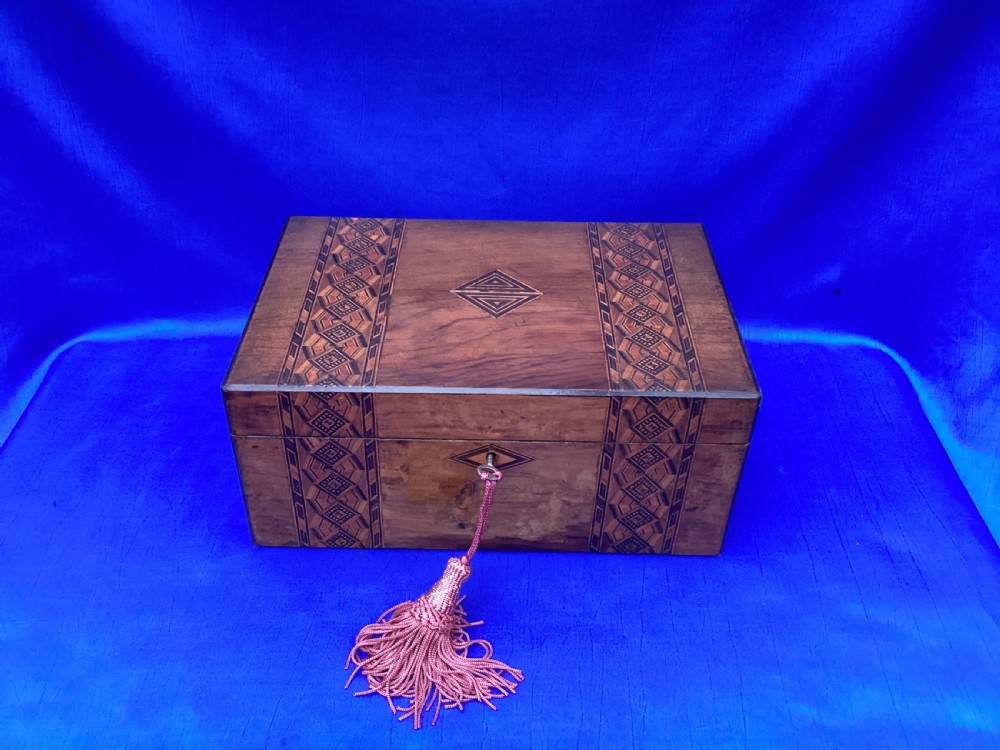 A rectangular Victorian walnut keepsake box featuring geometric parquetry inlay bands, a diamond escutcheon, and a key with a pink tassel. View II