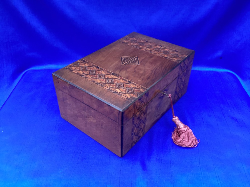 A rectangular Victorian walnut keepsake box featuring geometric parquetry inlay bands, a diamond escutcheon, and a key with a pink tassel. View III