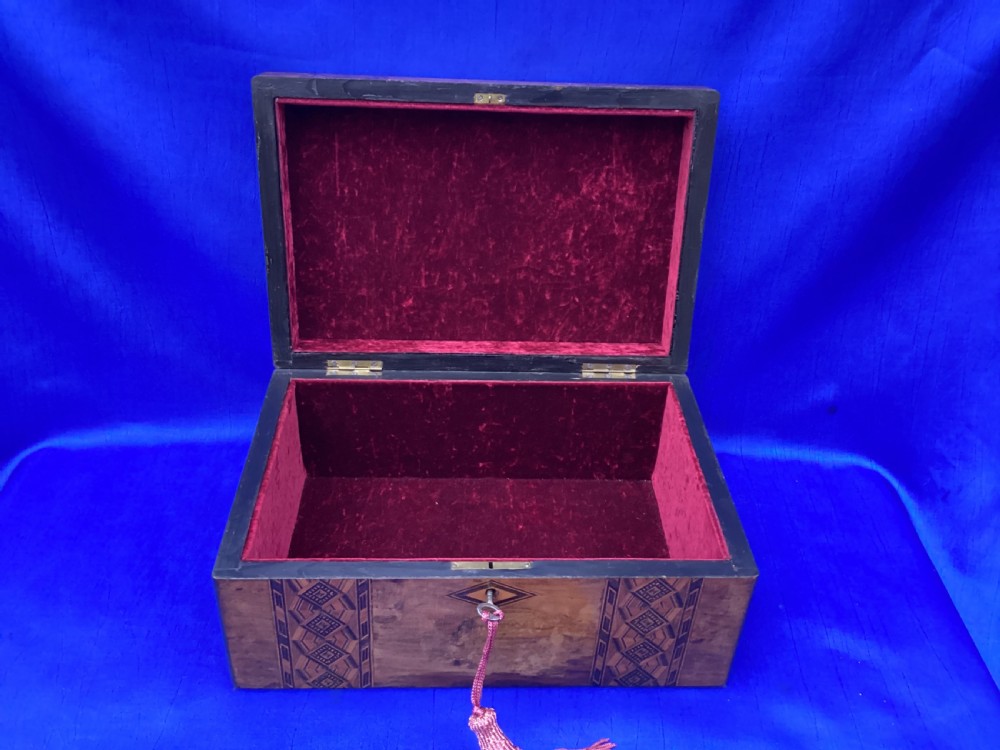 A rectangular Victorian walnut keepsake box featuring geometric parquetry inlay bands, a diamond escutcheon, and a key with a pink tassel. View IV