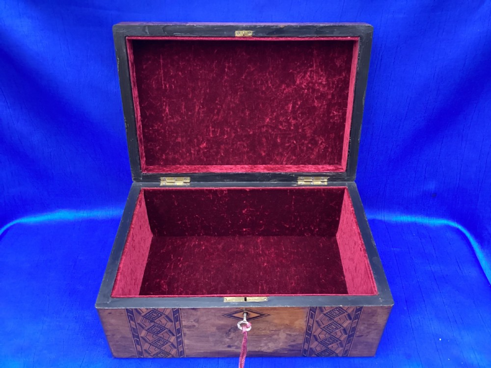 A rectangular Victorian walnut keepsake box featuring geometric parquetry inlay bands, a diamond escutcheon, and a key with a pink tassel. View V