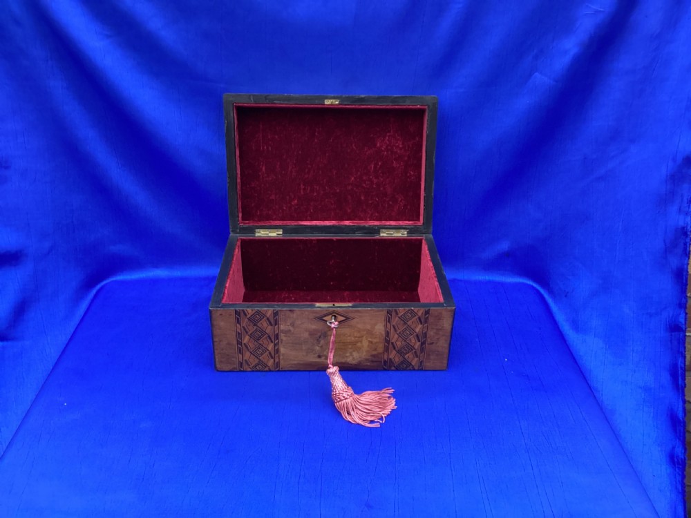 A rectangular Victorian walnut keepsake box featuring geometric parquetry inlay bands, a diamond escutcheon, and a key with a pink tassel. View VI
